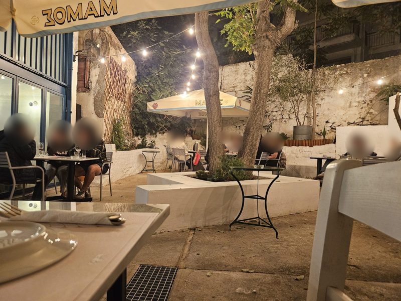 The courtyard of Vaggelis & Alekos in Neos Kosmos at night, string lights over tables under the trees